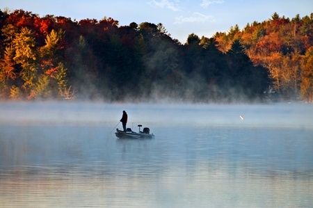 man fishing on a boat surrounded by fall foliage
