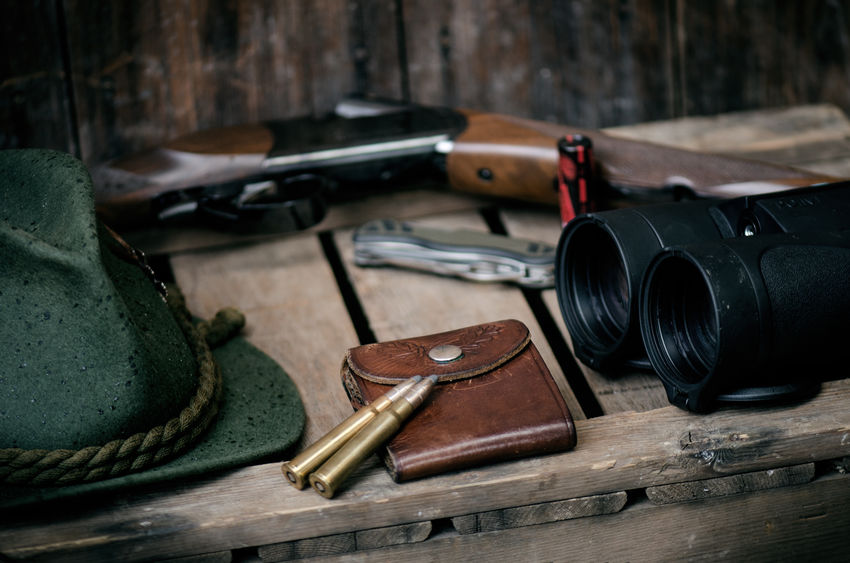 Professional hunters equipment for hunting. Detail on the ammunition. Wooden black background with rifle, hat, and other equipment for hunting.